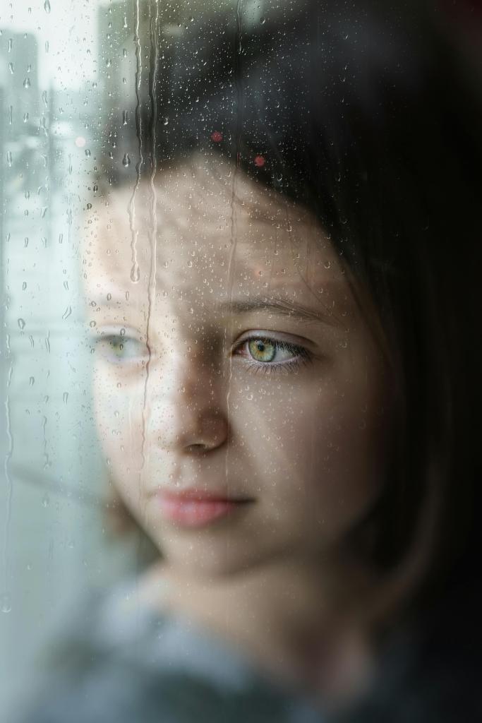 Enfant regardant par une fenetre, lumiere grise, ambiance melancolique — origine de la honte dans l'enfance