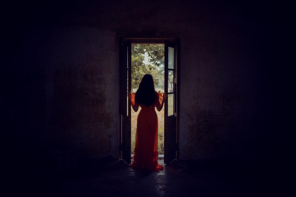 Femme de dos sur le seuil d'une porte entrouverte laissant entrer la lumière, illustrant le moment difficile de la décision de partir d'une relation toxique.