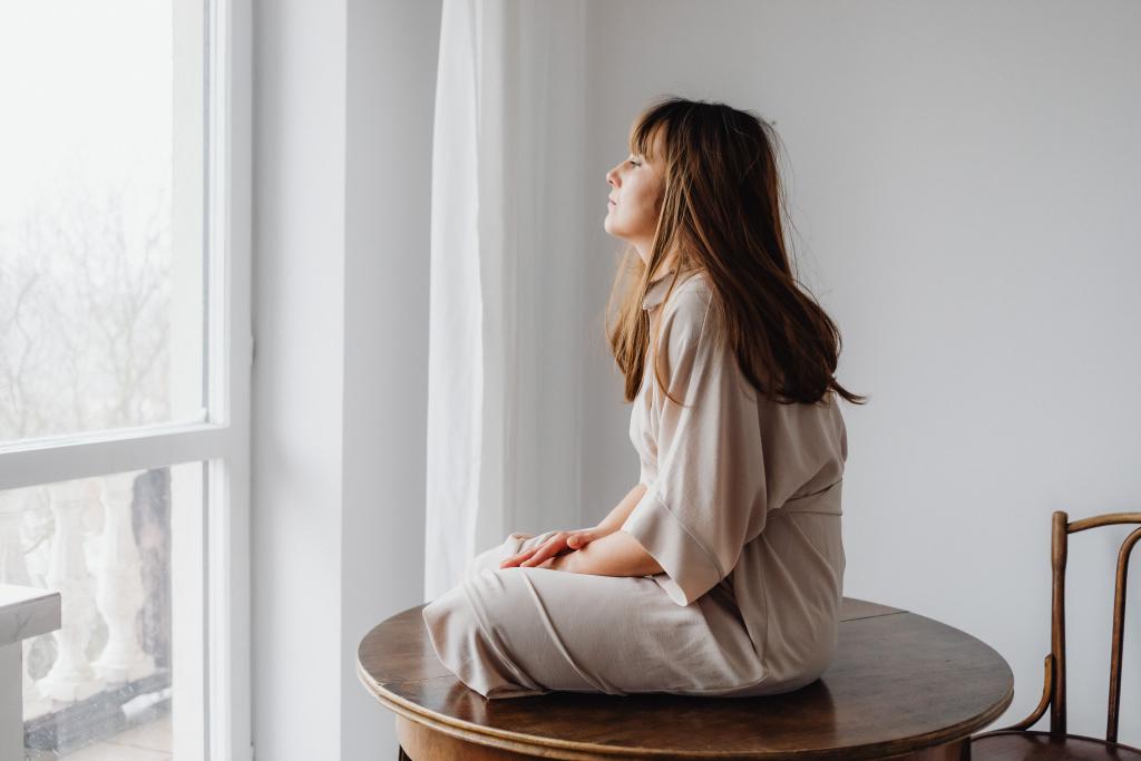 Femme assise dans un espace lumineux et calme, dans une attitude de recueillement, illustrant la reconnexion à ses besoins psychologiques profonds.